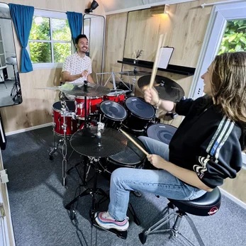 Drumleraar en leerling drummen samen in pipowagen